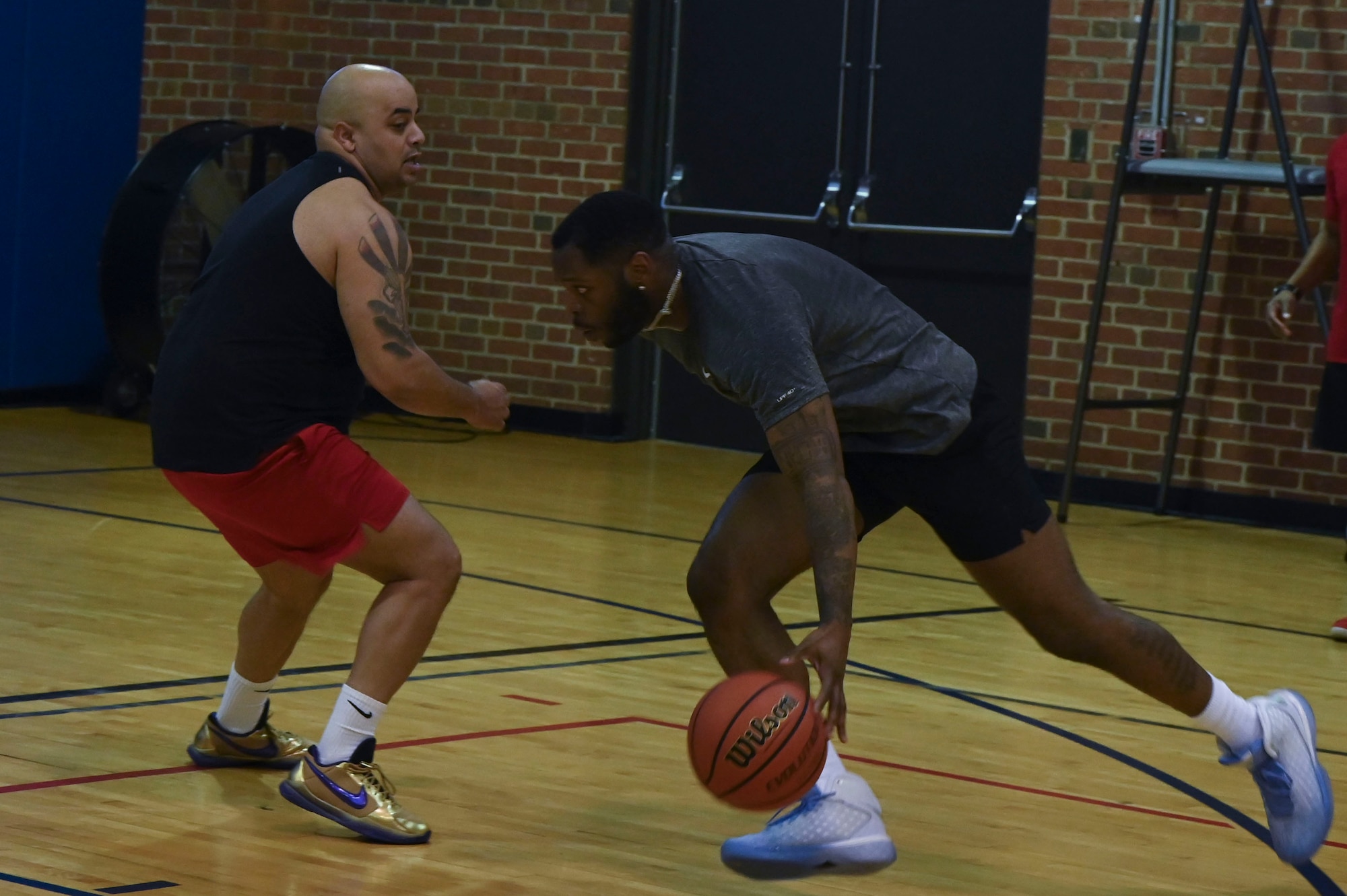 One man dribbles a basketball past another in a gymnasum.