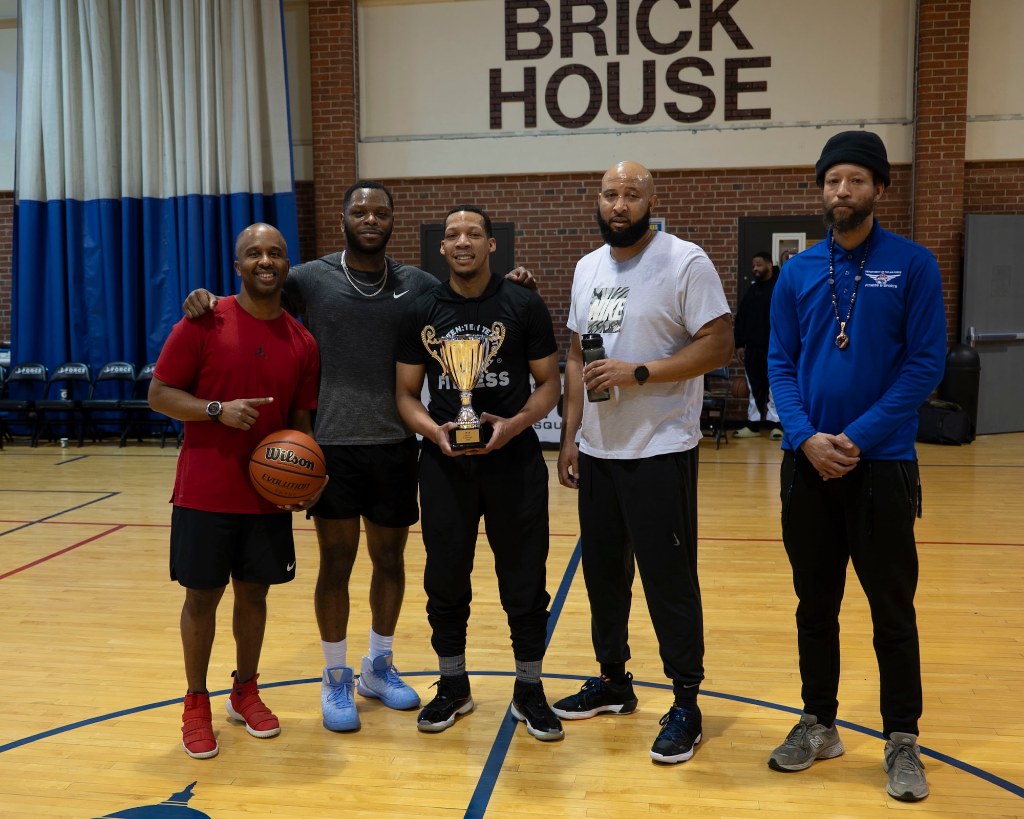 Five men stand with a single trophy in a gymnasium.