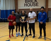 Five men stand with a single trophy in a gymnasium.