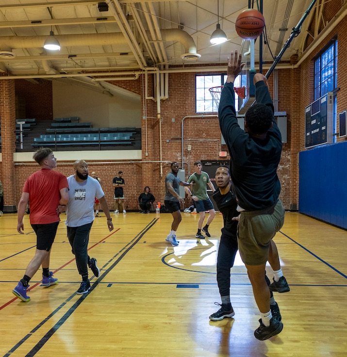 An airman shoots a basketball as others watch, vying for a rebound position.