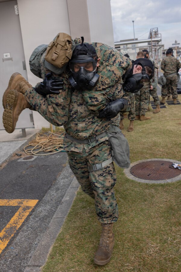 U.S. Marine Corps Lance Cpl. Roger AguilarGarcia, a power line mechanic with Marine Aerial Refueler Transport Squadron (VMGR) 152, Marine Aircraft Group 12, 1st Marine Aircraft Wing, and a native of San Bernardino, California, conducts a fireman’s carry on a simulated casualty during chemical, biological, radiological, and nuclear (CBRN) training at Marine Corps Air Station Iwakuni, Japan, Nov. 24, 2025. CBRN training is crucial for Marines to remain capable, confident and operation ready in any environment. (U.S. Marine Corps photo by Lance Cpl. Ella Cadby)