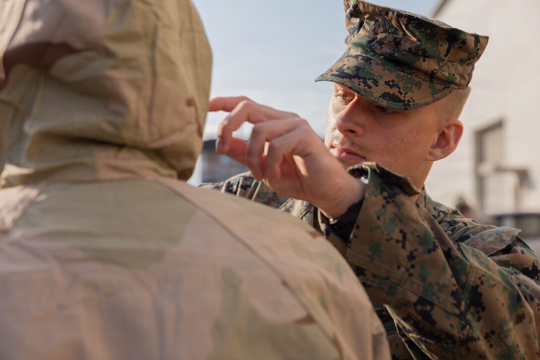 U.S. Marine Corps Lance Cpl. Christopher Benon, a chemical, biological, radiological, and nuclear (CBRN) specialist with Marine Wing Support Squadron (MWSS) 171, Marine Aircraft Group 12, 1st Marine Aircraft Wing, assists a Marine in putting on his gear at Marine Corps Air Station Iwakuni, Japan, Nov. 25, 2025. CBRN training is crucial for Marines to remain capable, confident and operation ready in any environment. (U.S. Marine Corps photo by Lance Cpl. Ella Cadby)