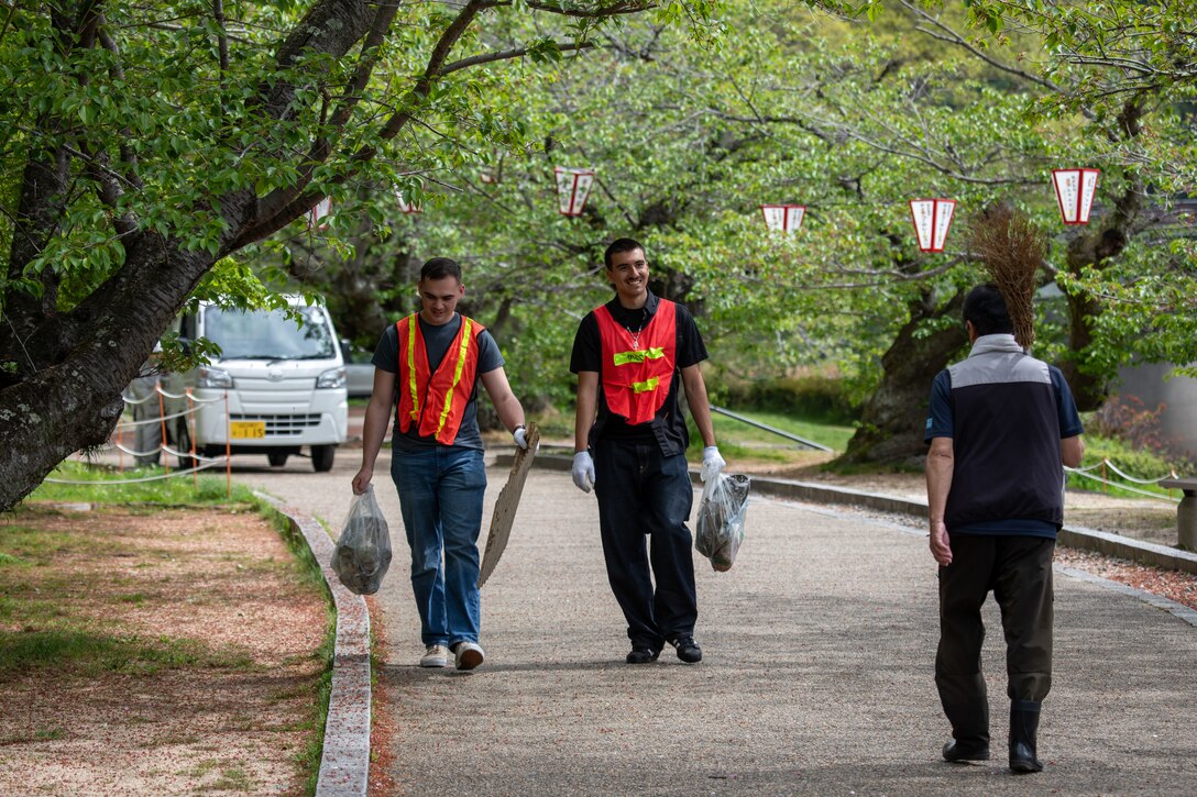 U.S. Marine Corps Lance Cpl. Aidan Montalvo, left, a native of California, and Cpl. Nicholas Brooks, a native of Nevada, both expeditionary firefighting and rescue specialists with Aircraft Rescue and Firefighting, Headquarters and Headquarters Squadron, Marine Corps Air Station Iwakuni, interact with a local during a clean-up at the Kintaikyo Bridge, Iwakuni, Japan, April 21, 2025. The Marine Corps Community Services Iwakuni, Single Marine Program hosted a bridge clean-up as part of the SMP Days of Service, a five-day series of events where service members from Marine Corps Air Station Iwakuni volunteer to build stronger relationships and give back to the community. (U.S. Marine Corps photo by Sgt. Randall Whiteman)