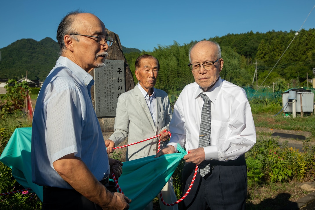 Yozo Kudo, a Japanese historian, left, and Shigeaki Mori, right, a Japanese historian and Hiroshima atomic bombing survivor, pose for a group photo during an unveiling ceremony in Yanai, Japan, July 28, 2025. Mr. Mori is a prominent historian, and his work was critical in documenting the fate of the Lonesome Lady and her crew. (U.S. Marine Corps photo by Lance Cpl. Micah Taylor)
