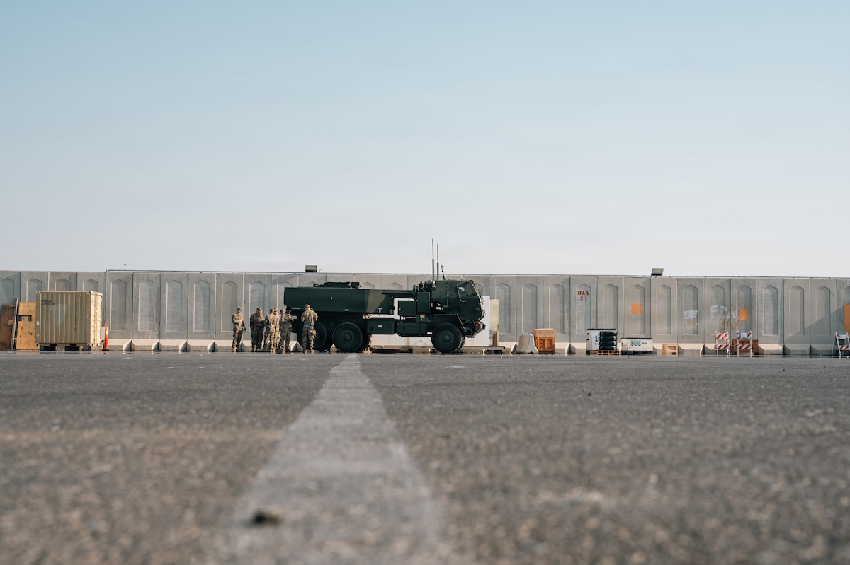 People stand around military vehicle