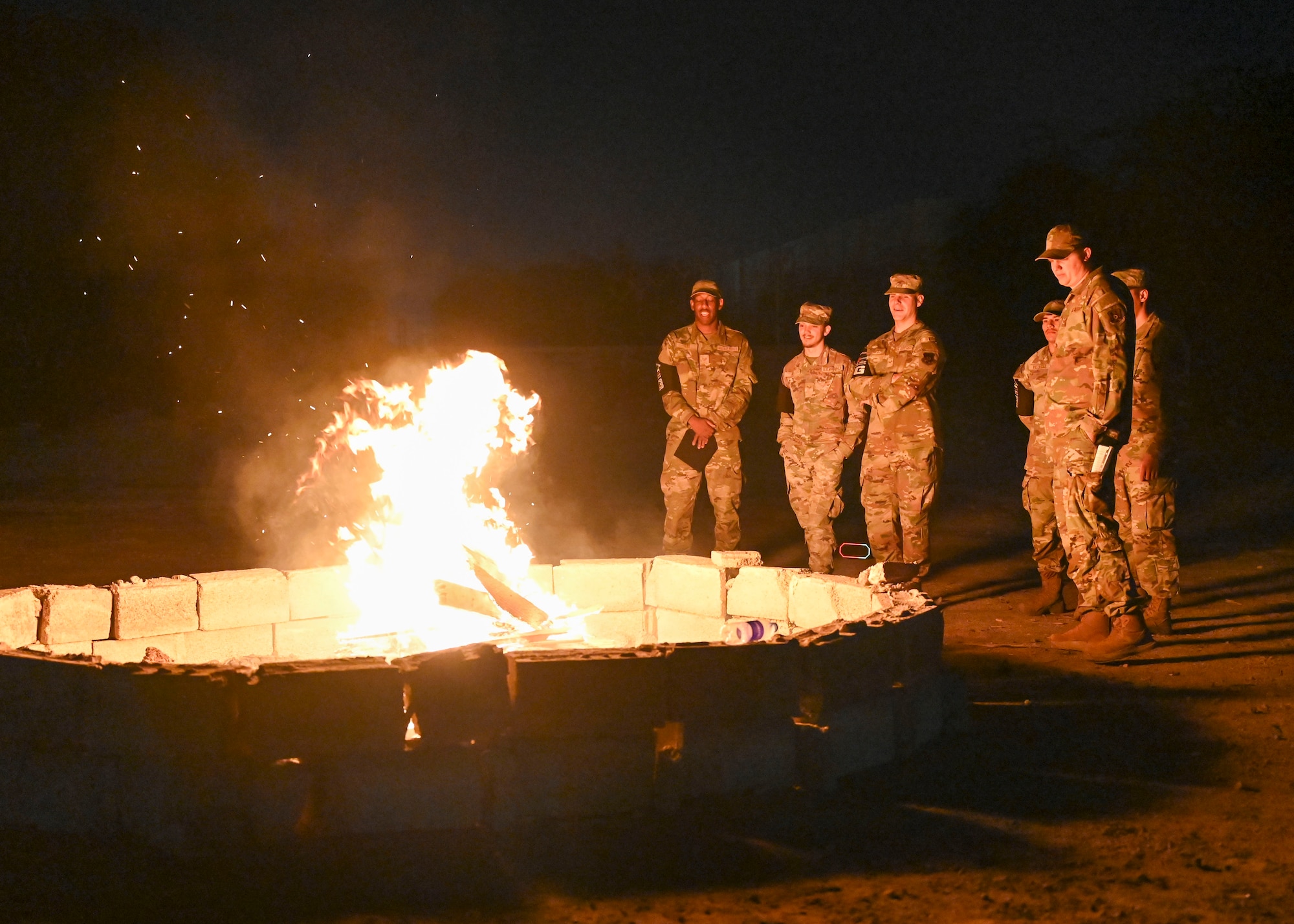 Men in military uniforms watch a small fire.