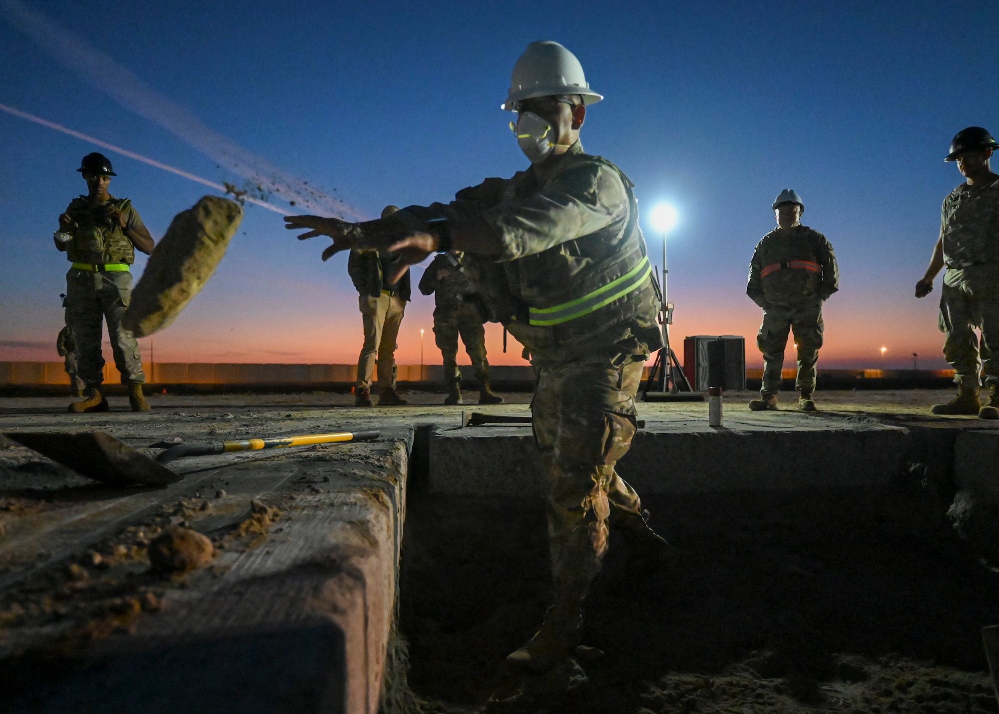 A man in a military uniform throws a chunk of concrete out of a hole.