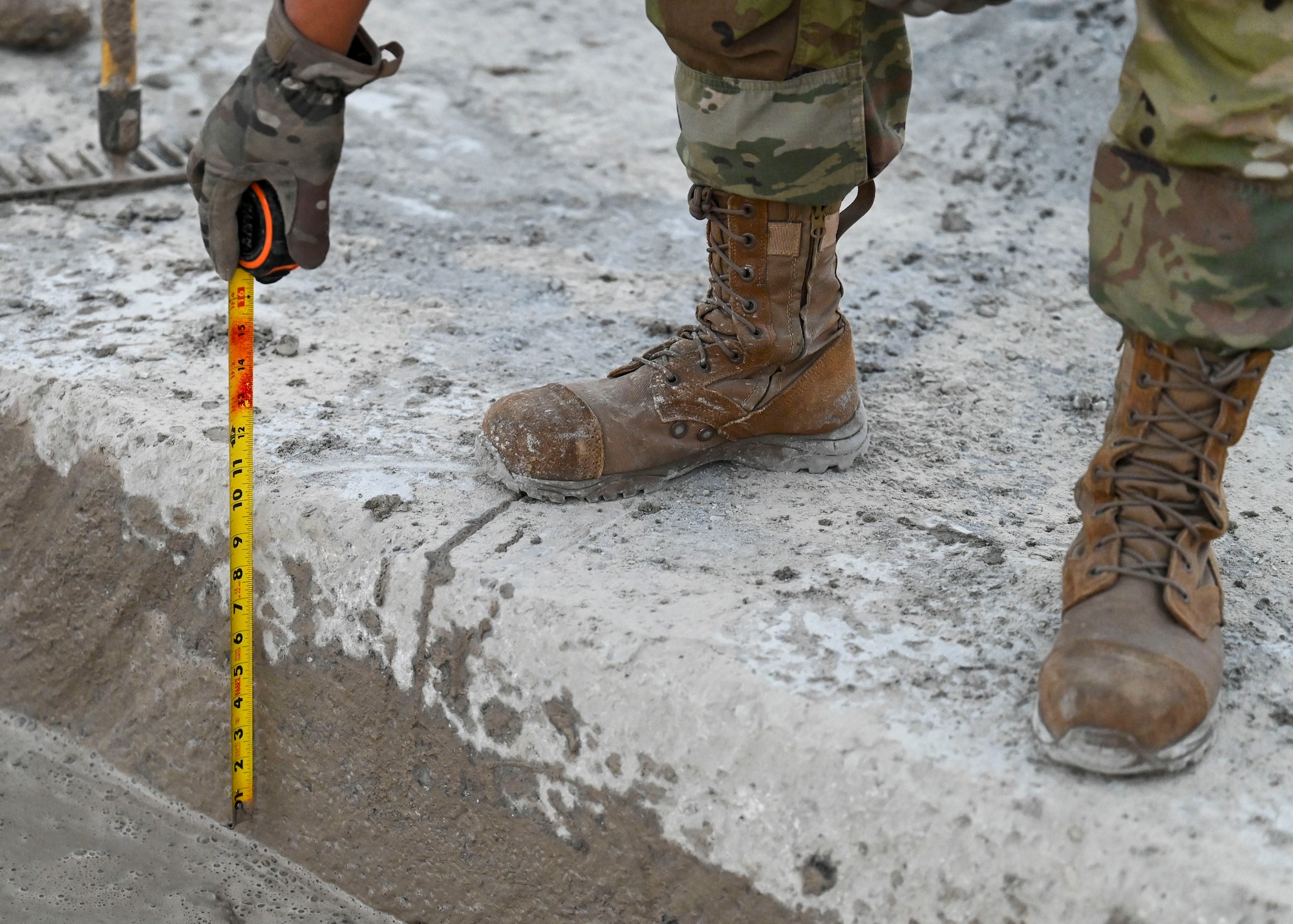 A man in a military uniform uses a tape measure to calculate how much more concrete is needed to fill a hole.