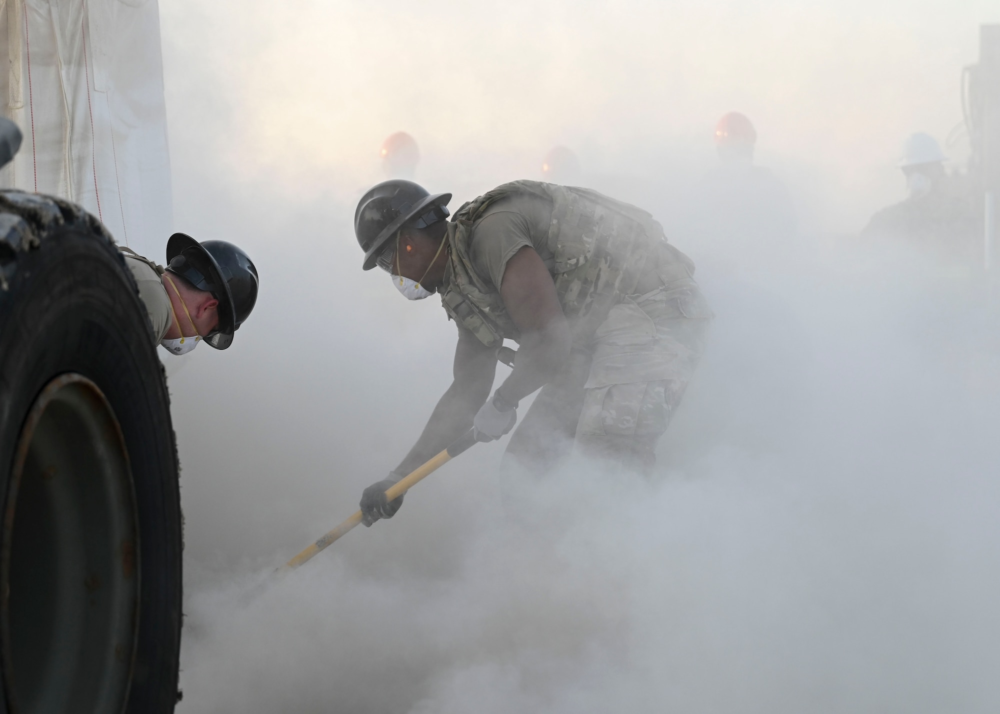 Men in military masks distribute conrete using tools while cement powder surrounds them.