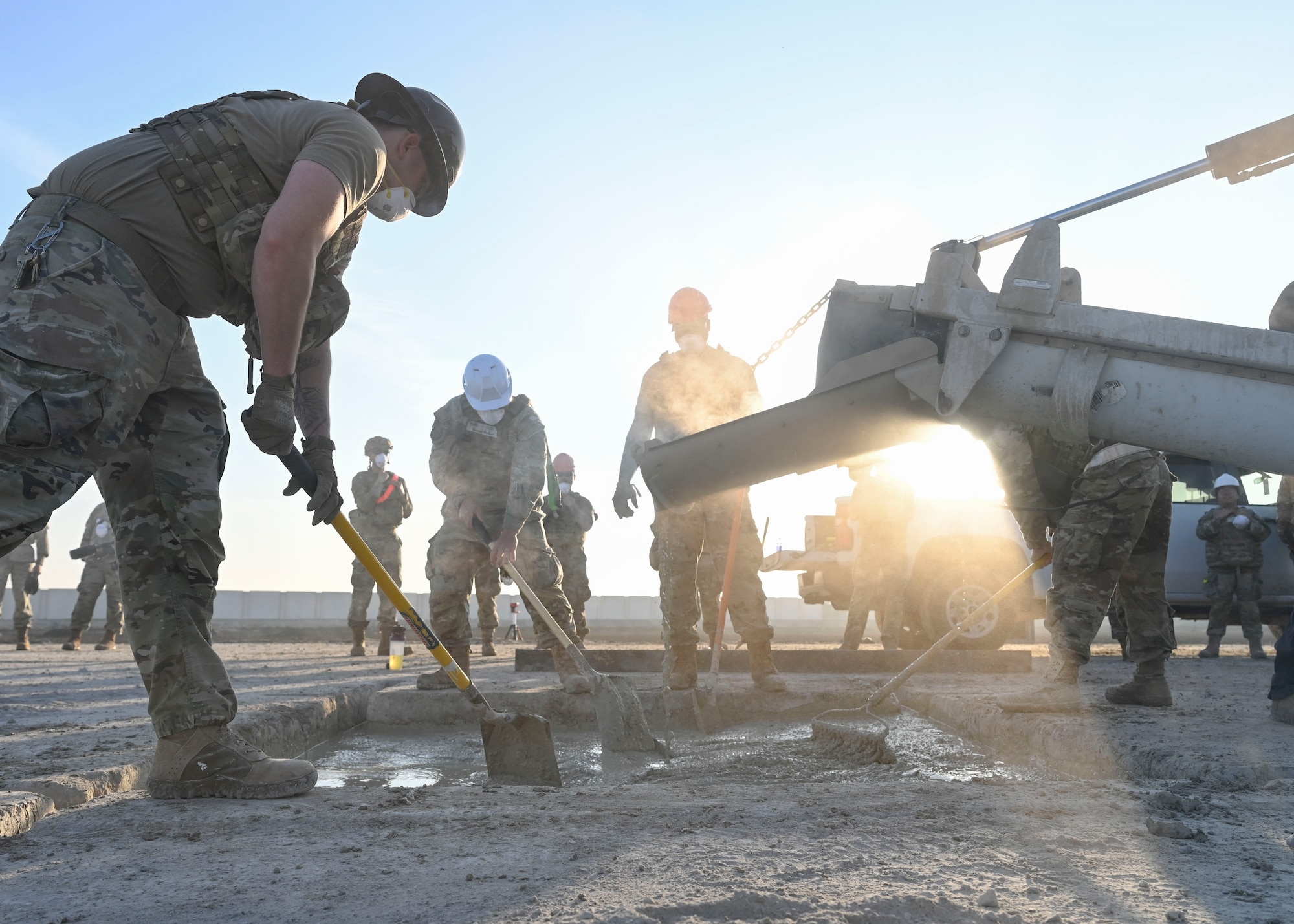 Men in military uniforms distribute concrete with shovels and rakes.