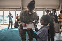 U.S. Air Force Senior Airman Amal Djezzar, an Air Forces Central (AFCENT) arabic translator for the Bahrain International Airshow, signs a little girl’s notebook at a “Meet the Pilot”