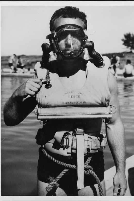 A man in a swimsuit, a face mask and other underwater equipment around his chest and waist poses for a photo.