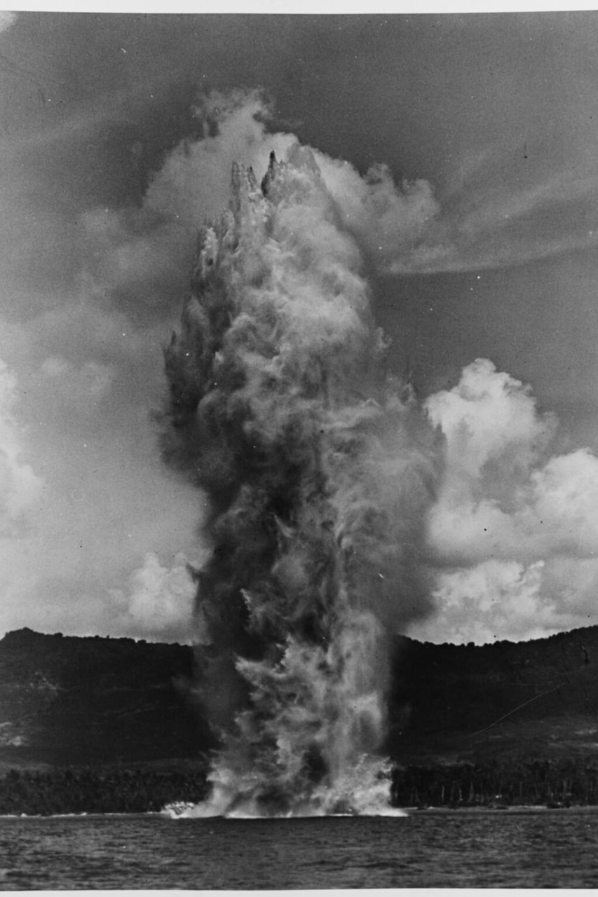 A massive plume of water shoots up from the ocean near an island beach.