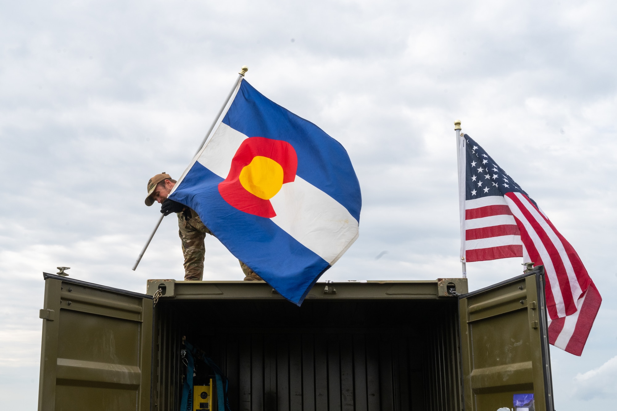 U.S. Air Force Staff Sgt. Ben Dragstrem, chemical, biological, radiological and nuclear enhanced response force package search and extraction team medic, 140th Medical Group, Detachment 1, secures the Colorado flag to a storage container during the Vigorous Warrior and Clean Care 2024 medical exercises, May 3, 2024, at Bakonykúti Training Area, Hungary.