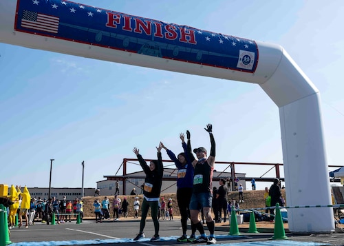 Three runners pose underneath the finish line blow up.