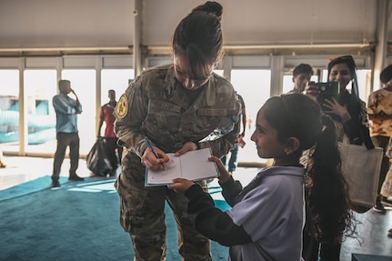 U.S. Air Force Senior Airman Amal Djezzar, an Air Forces Central (AFCENT) arabic translator for the Bahrain International Airshow, signs a little girl’s notebook at a “Meet the Pilot”