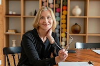 Smiling woman sits at a table while holding her glasses.