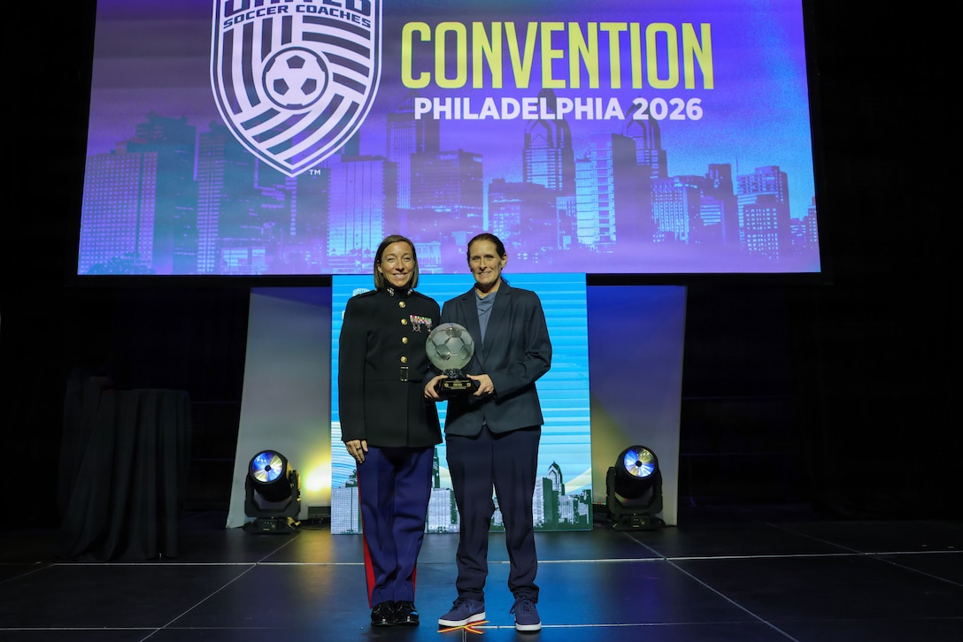 U.S. Marine Corps Maj. Jaime Goss, deputy G-1 manpower officer, 2nd Marine Logistics Group, II Marine Expeditionary Force, left, presents the 2026 Women’s Award of Excellence to Lisa Cole, American women's soccer coach and former player, and is currently a technical advisor for the Zambia women's national football team, at the Women’s Soccer Breakfast during the 2026 United Soccer Coaches Convention in Philadelphia, Jan. 17, 2026. Marine Corps Recruiting Command’s partnership with United Soccer Coaches offers the opportunity to develop new relationships with coaches to build trust and create a larger pool of advocates to access talented young men and women. (U.S. Marine Corps photo by Cpl. Brenna Ritchie).