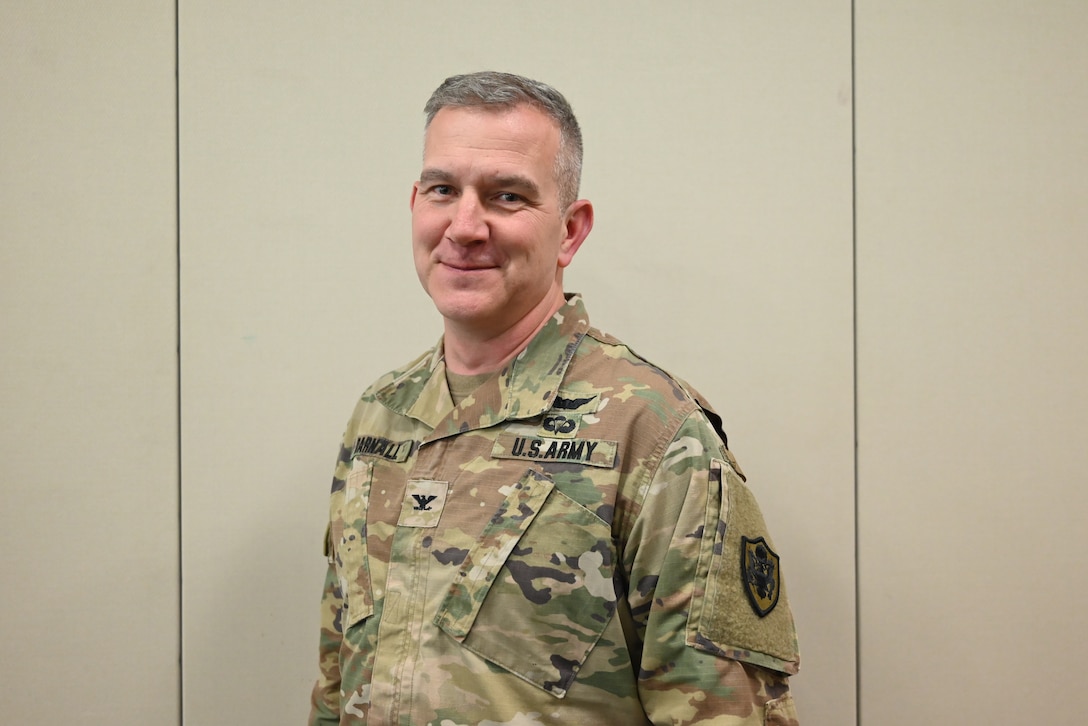 A smiling man wears an Army camouflage uniform
