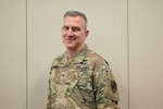 A smiling man wears an Army camouflage uniform