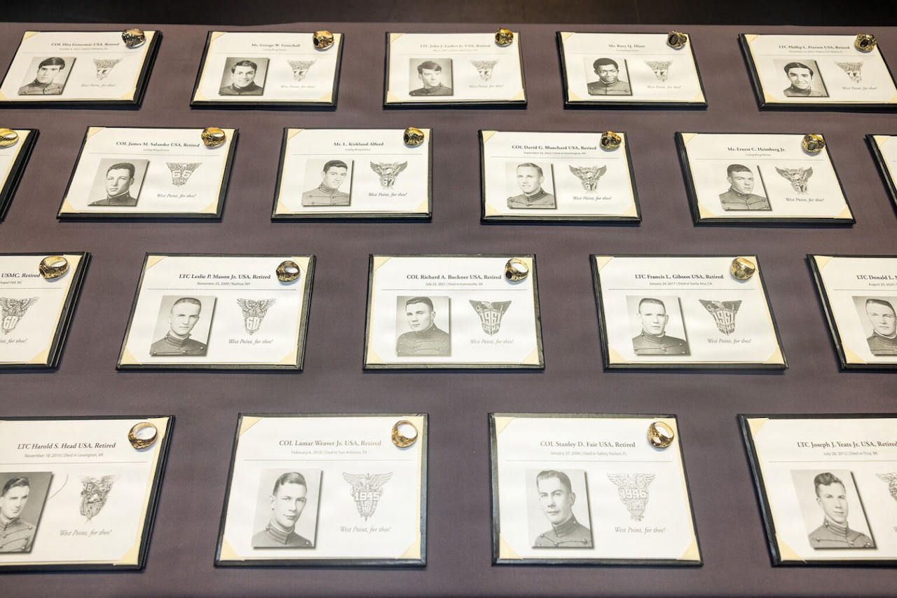 Black and white photos of men in military dress uniforms are displayed in rows on a table as gold rings sit on top of each photo.