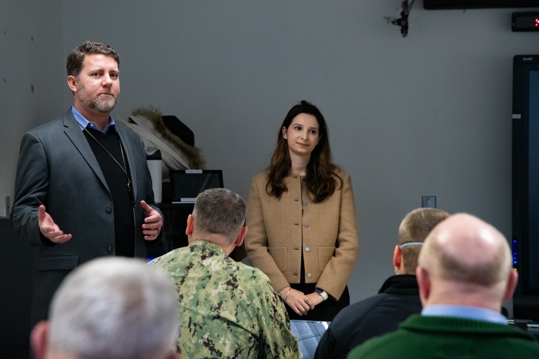 A man stands in front of a group of people in a conference room, speaking
