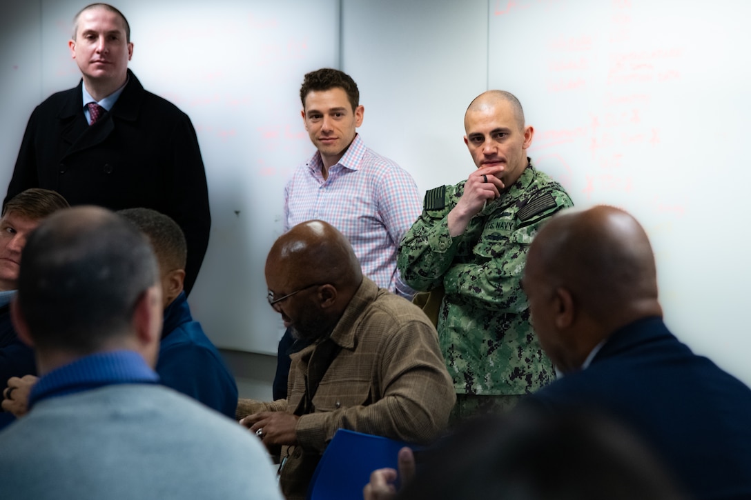 A group of people stand inside a conference room talking to each other.