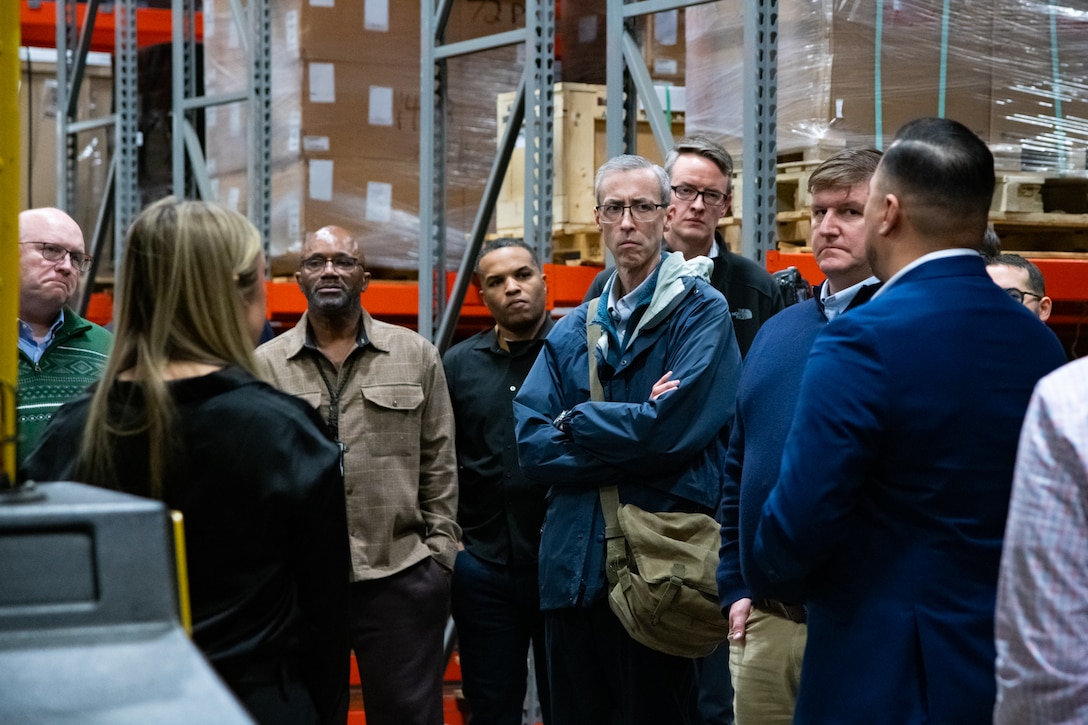 A group of people stand inside a warehouse talking to each other.