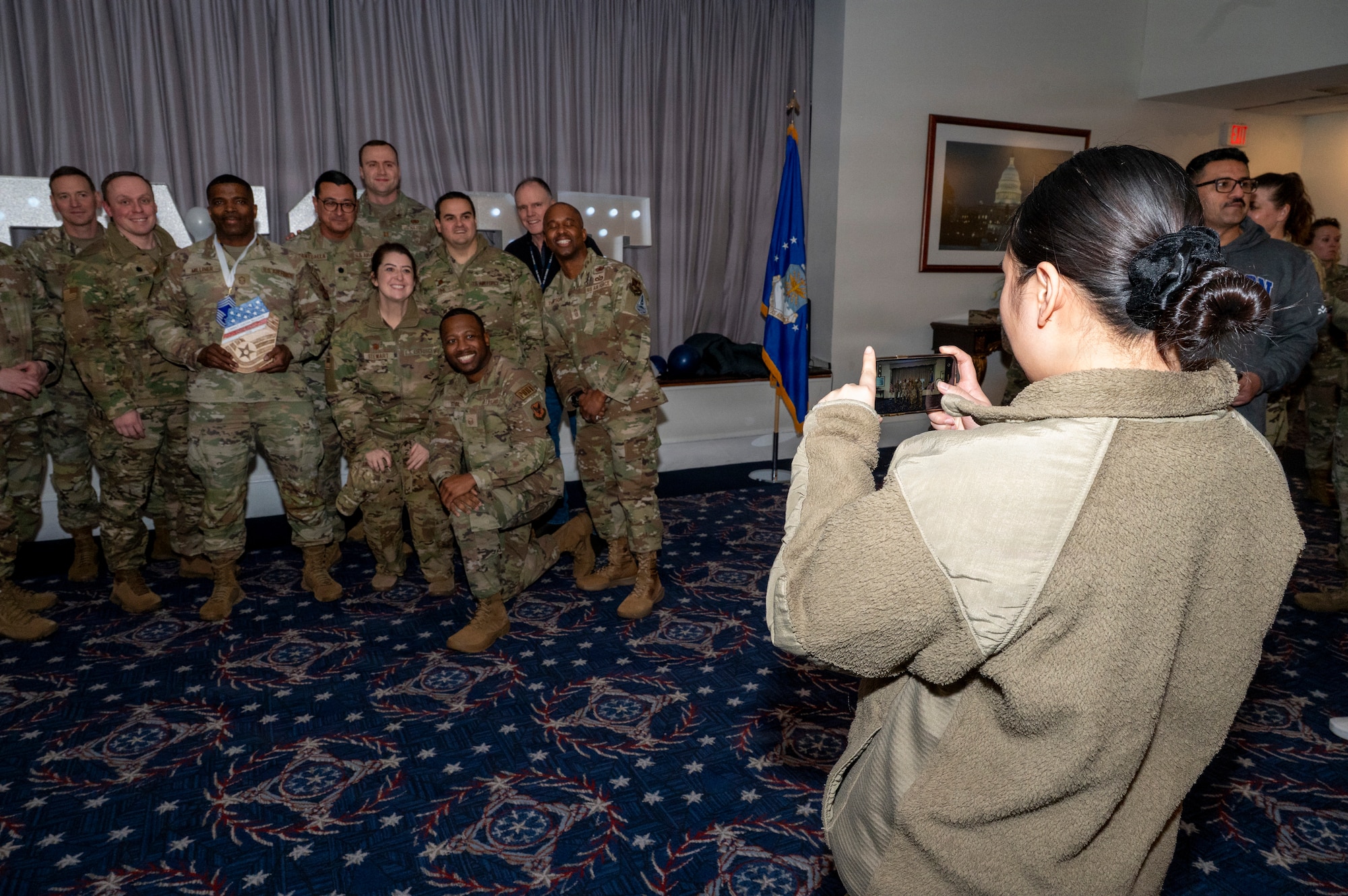 An audience member takes a photo of Senior Master Sgt. Juston Milliner, Office of Joint Chiefs of Staff, with colleagues during a chief master sergeant release party at Joint Base Anacostia-Bolling, Washington, D.C., Jan. 15, 2026. These individuals achieved the rank of chief master sergeant which is a mark of distinction, recognizing years of dedication and the ability to lead at the highest levels of the enlisted force. (U.S. Air Force photo by Hayden Hallman)