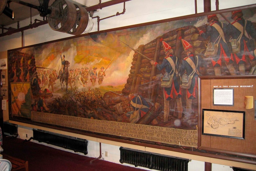 A large painting depicting people in Revolutionary War uniforms hangs on a white brick wall.