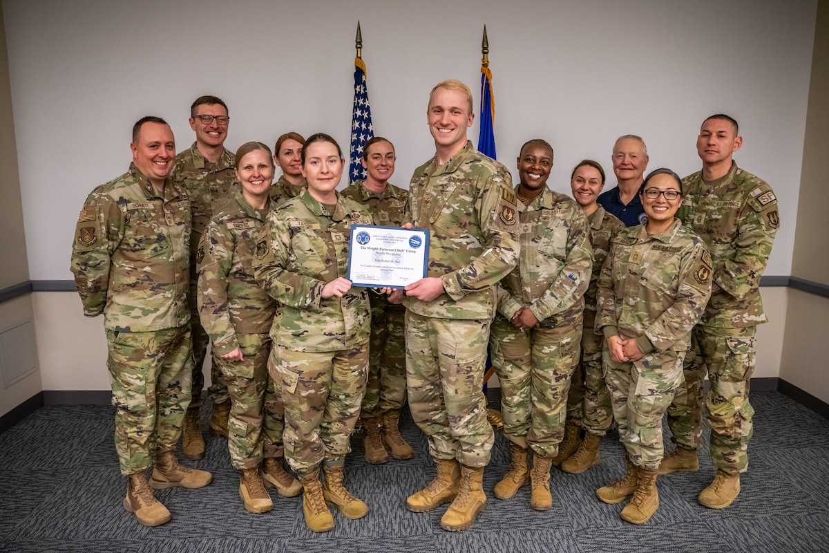 A large group photo of military members, wearing camouflage uniforms, the center two people holding an award certificate