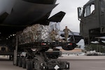Service members offload cargo from a military airplane using heavy equipment machinery.