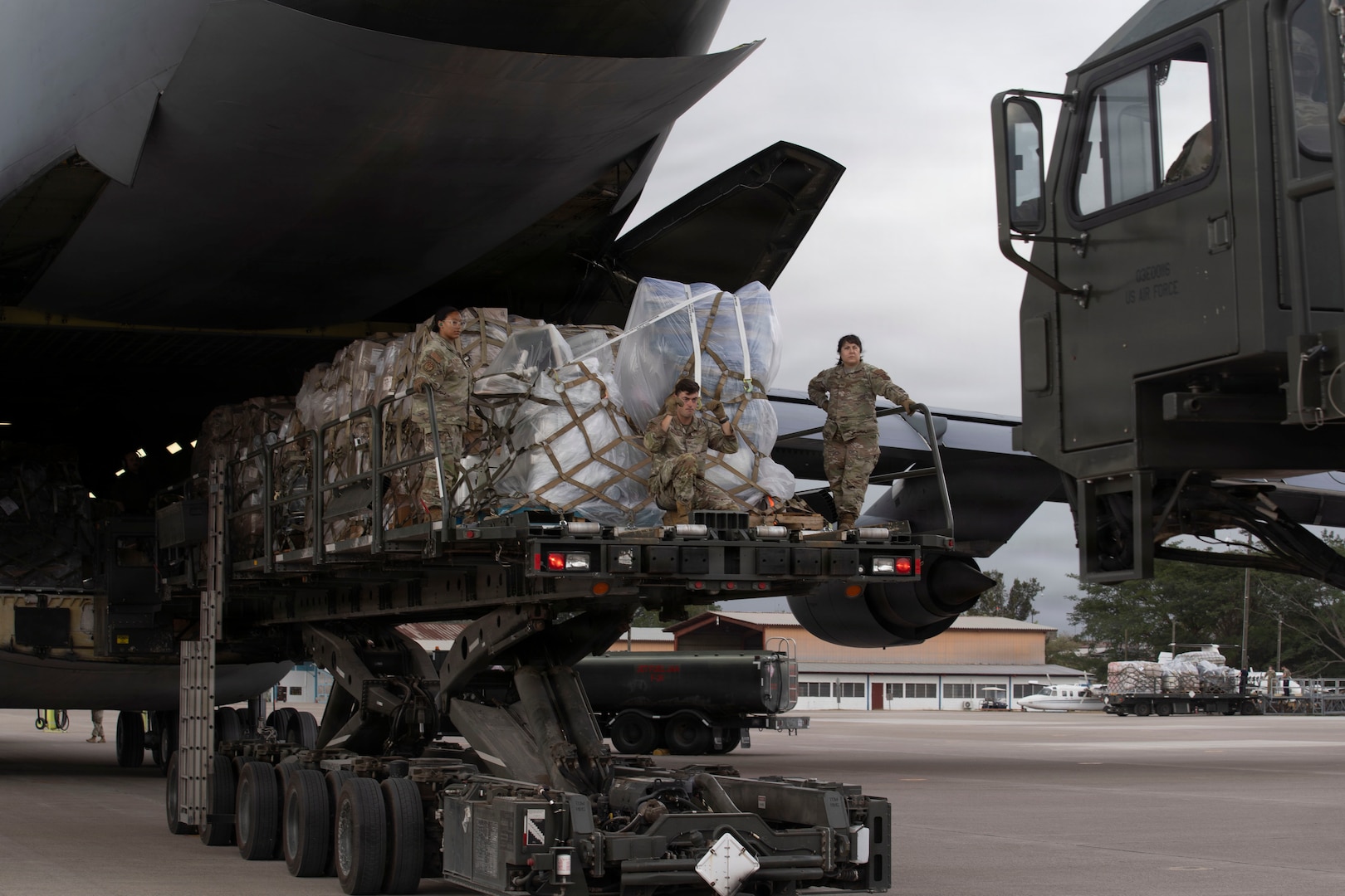 Service members offload cargo from a military airplane using heavy equipment machinery.