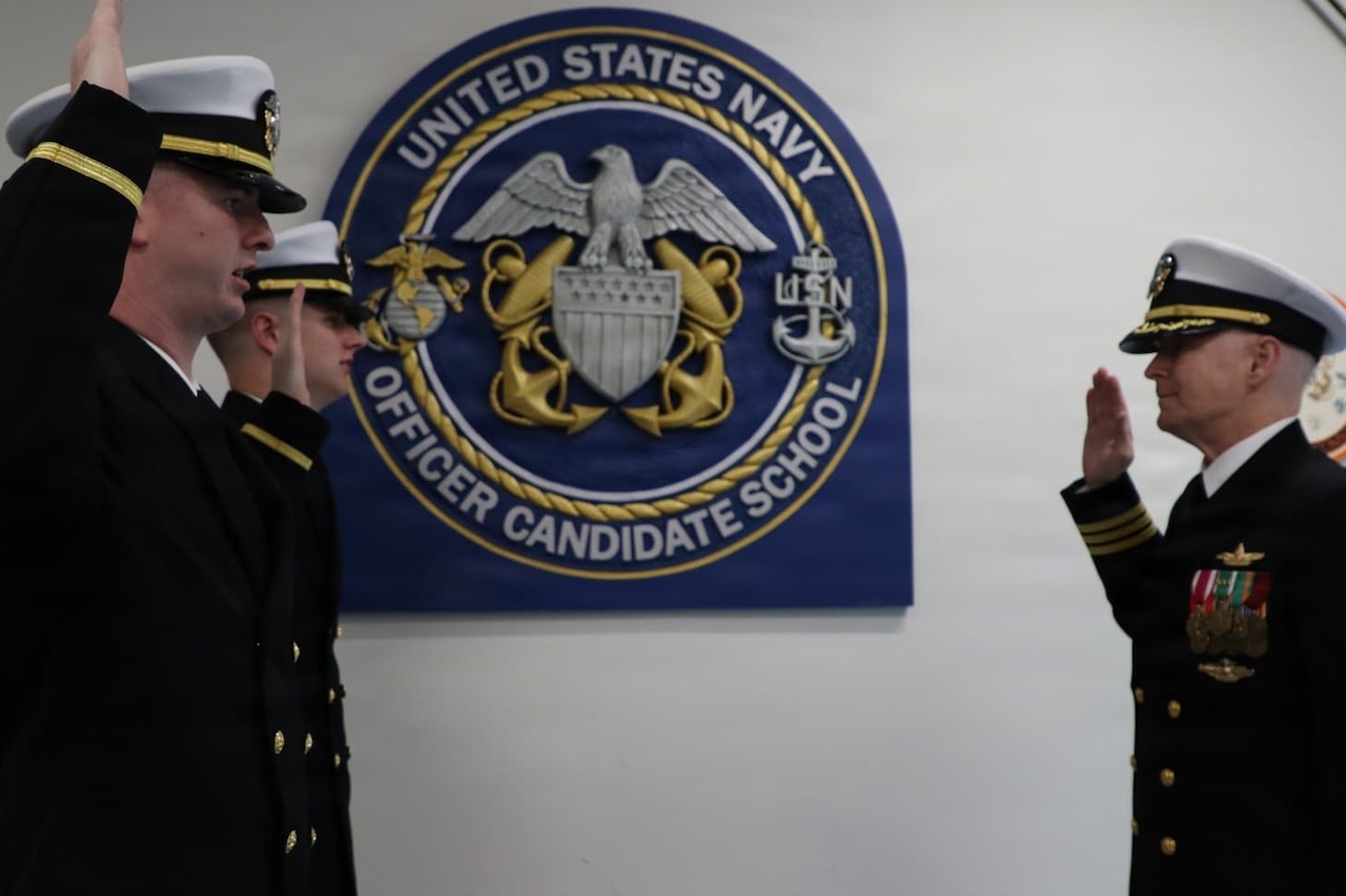 A U.S. Navy officer administers the oath of office to two other officers; all three men are in dress uniforms with their right hands raised.