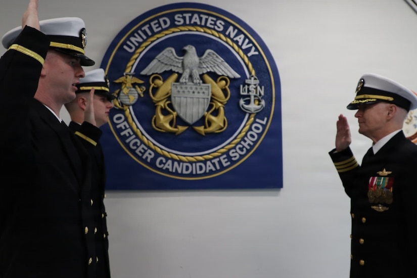 A U.S. Navy officer administers the oath of office to two other officers; all three men are in dress uniforms with their right hands raised.