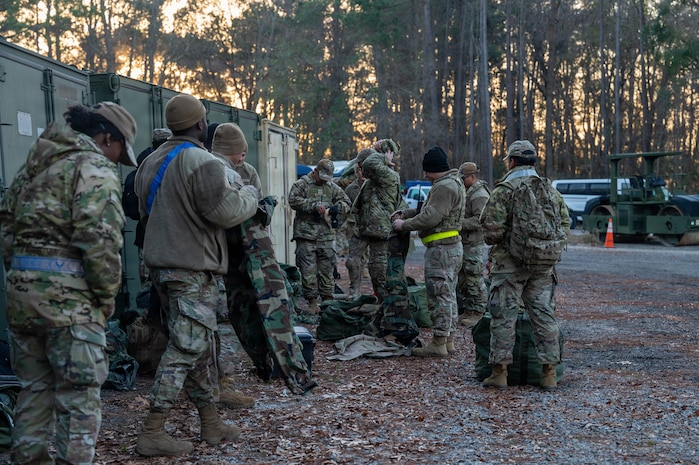 A group of Airmen check equipment with equipment and storage in the background.