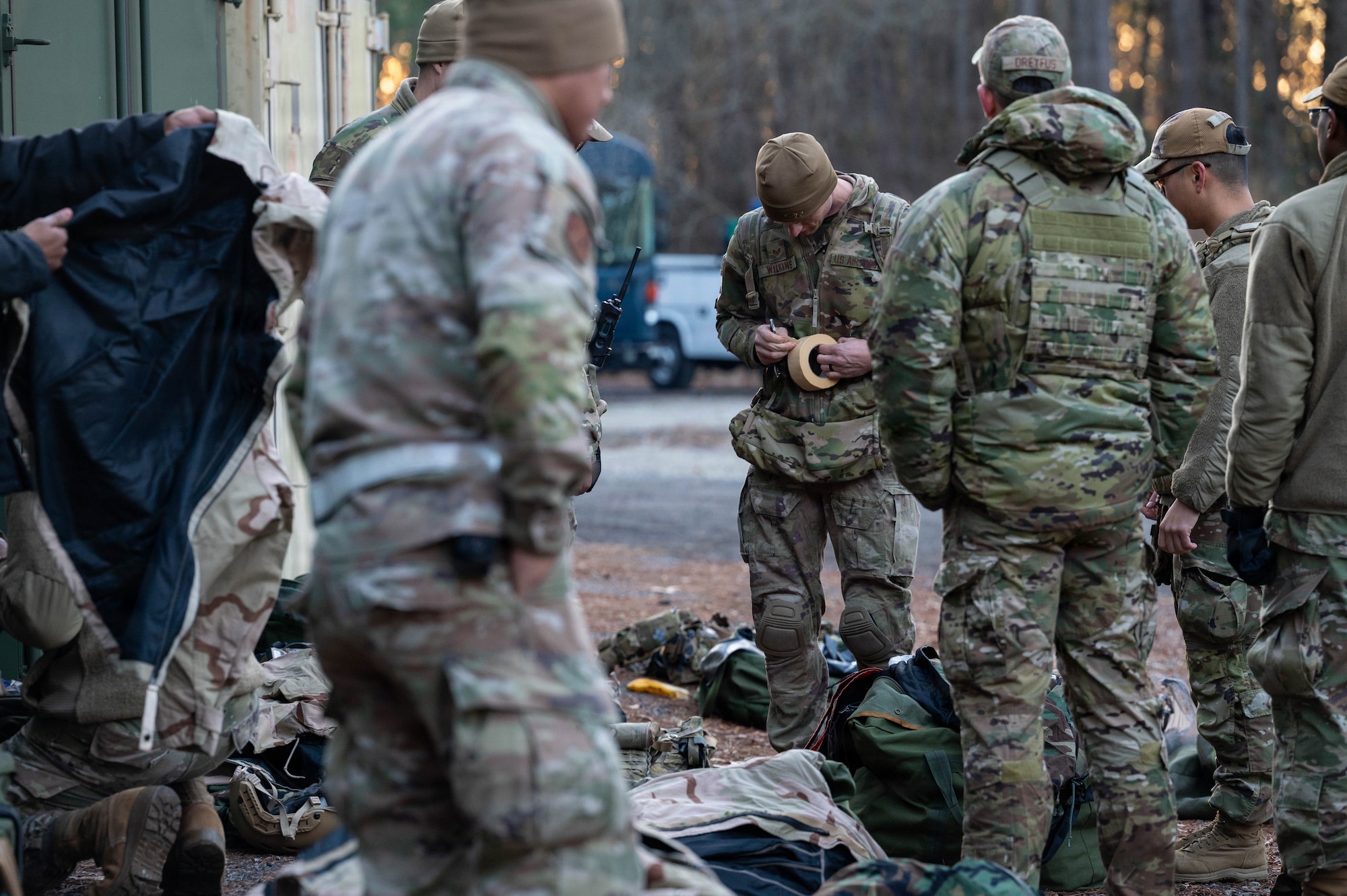 A group of Airmen check gear with equipment and storage in the background.