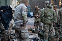 A group of Airmen check gear with equipment and storage in the background.