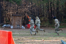 Three Airmen run to the left across a clearing with plastic weapons in hand.