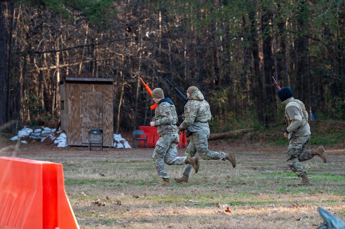 Three Airmen run to the left across a clearing with plastic weapons in hand.