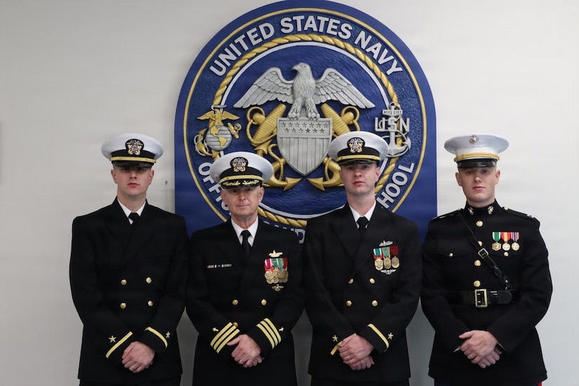 Four men in U.S. Navy and U.S. Marine Corps uniforms stand together for a group photograph indoors.