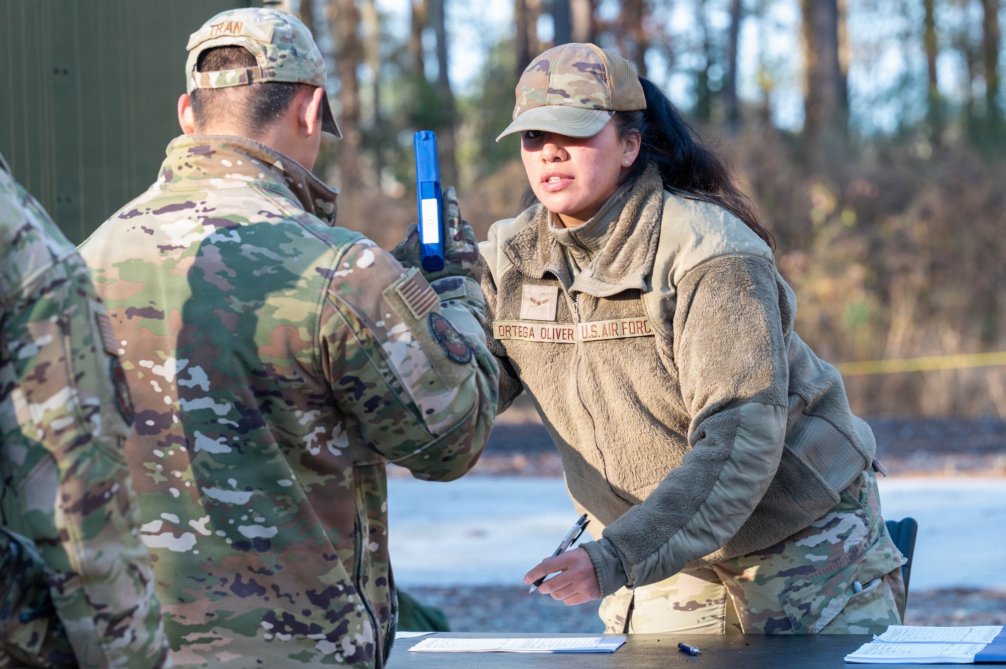 Two Airmen stand over a table, one holding a blue plastic weapon and the other writing on a paper.