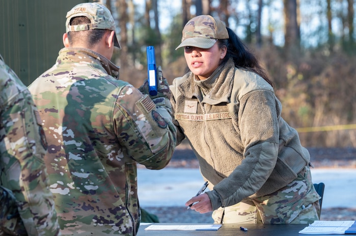 Two Airmen stand over a table, one holding a blue plastic weapon and the other writing on a paper.