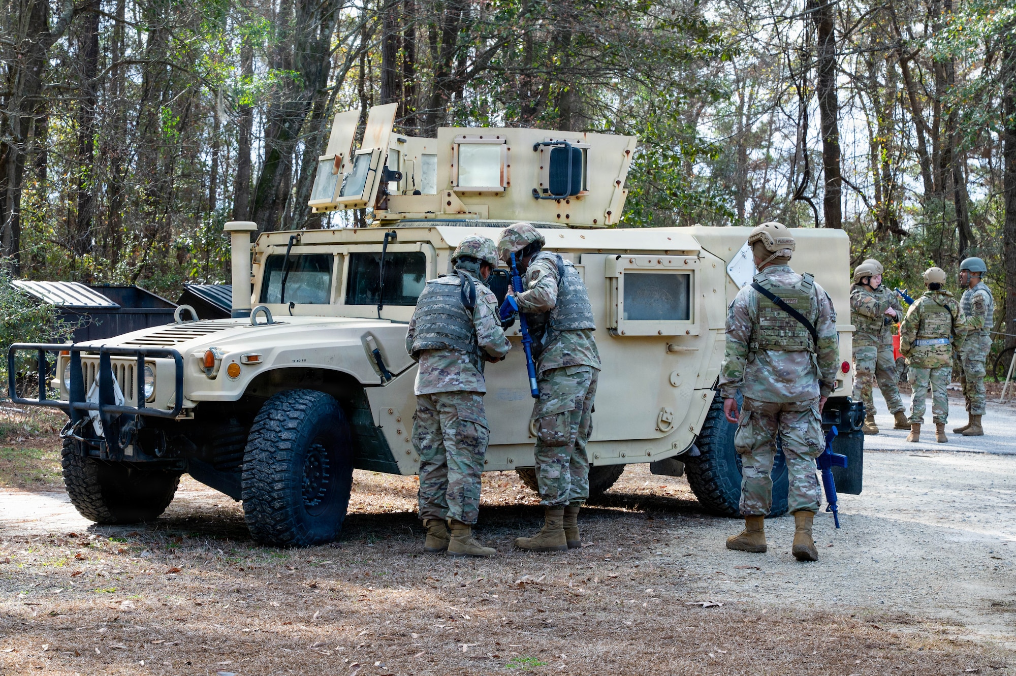 Airmen stand in front of a tan Humvee, two peering in the window and one standing off to the right.