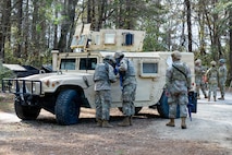 Airmen stand in front of a tan Humvee, two peering in the window and one standing off to the right.