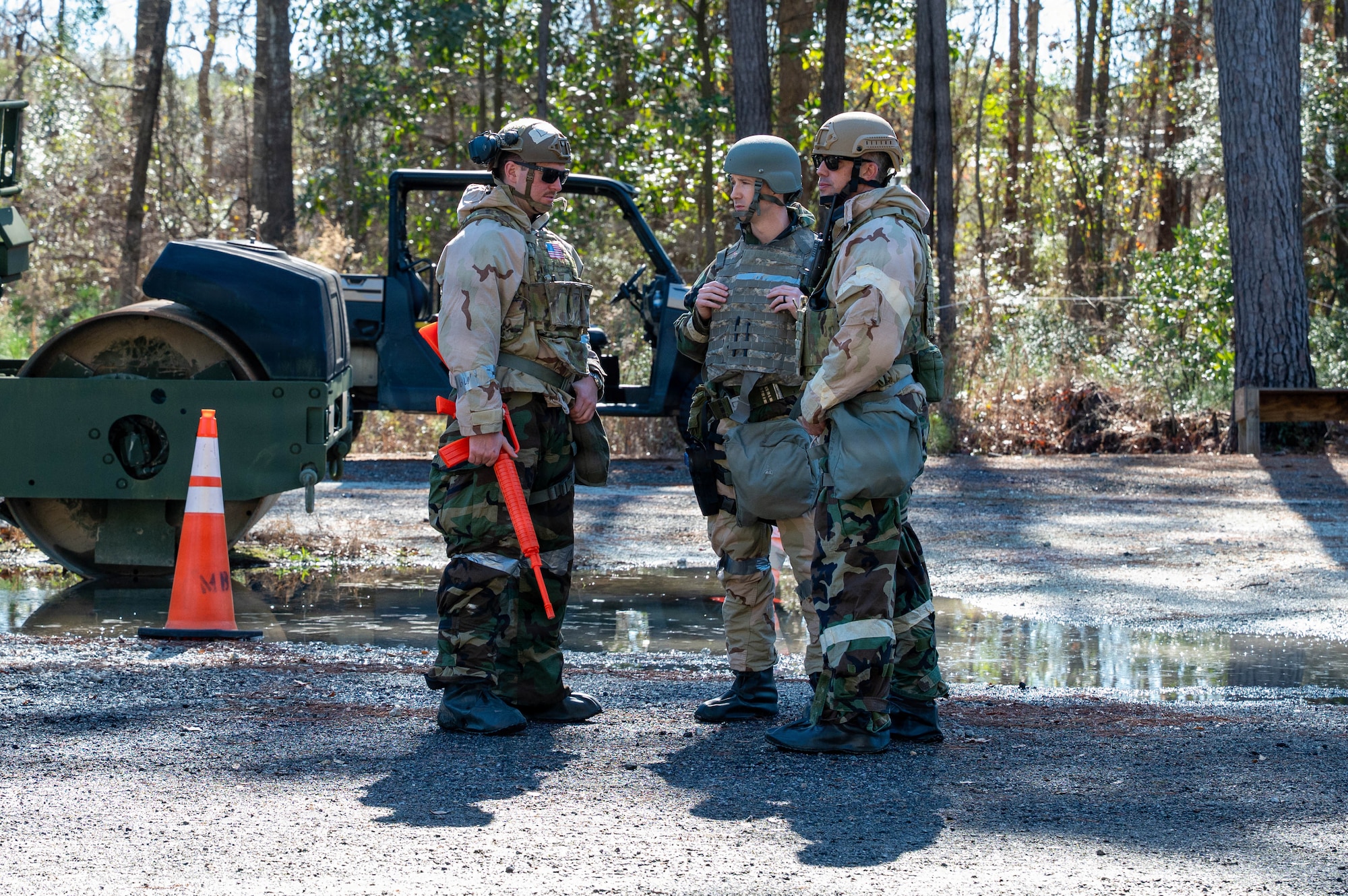 Three Airmen stand in a clearing with equipment in the background.