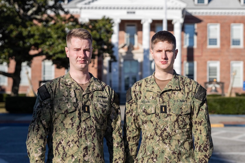 Two sailors stand side-by-side outside in front of building during a sunny day.