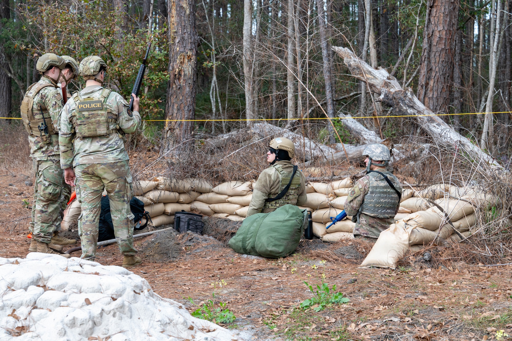 Four Airmen stand around a hole in the ground surrounded by sand bags.