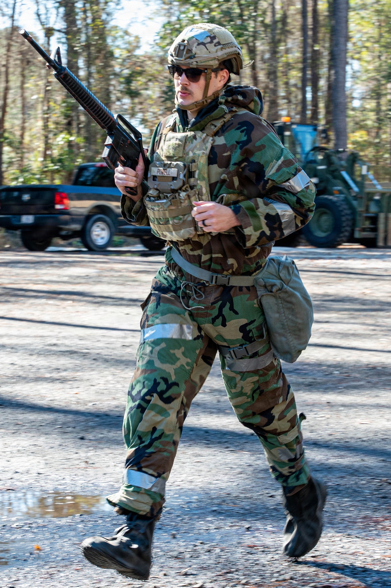 An Airman holding a training weapon runs across a clearing.