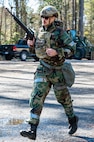 An Airman holding a training weapon runs across a clearing.
